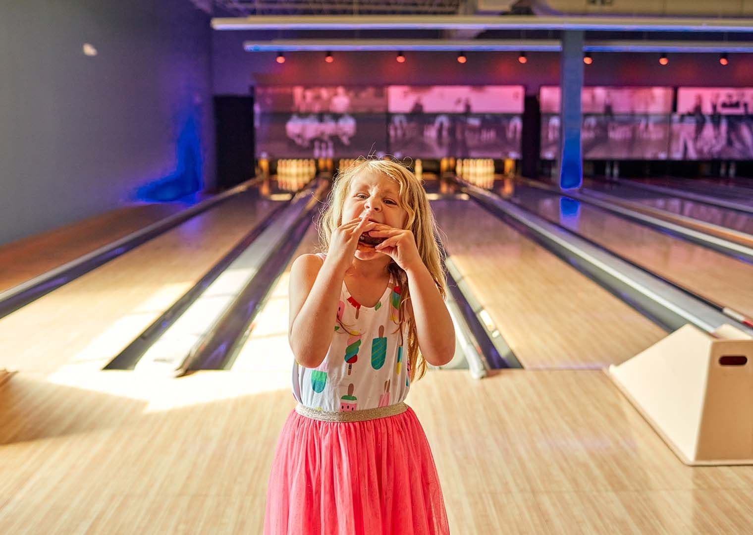 Little girl eating a burger on the bowling lanes at Pinstripes.