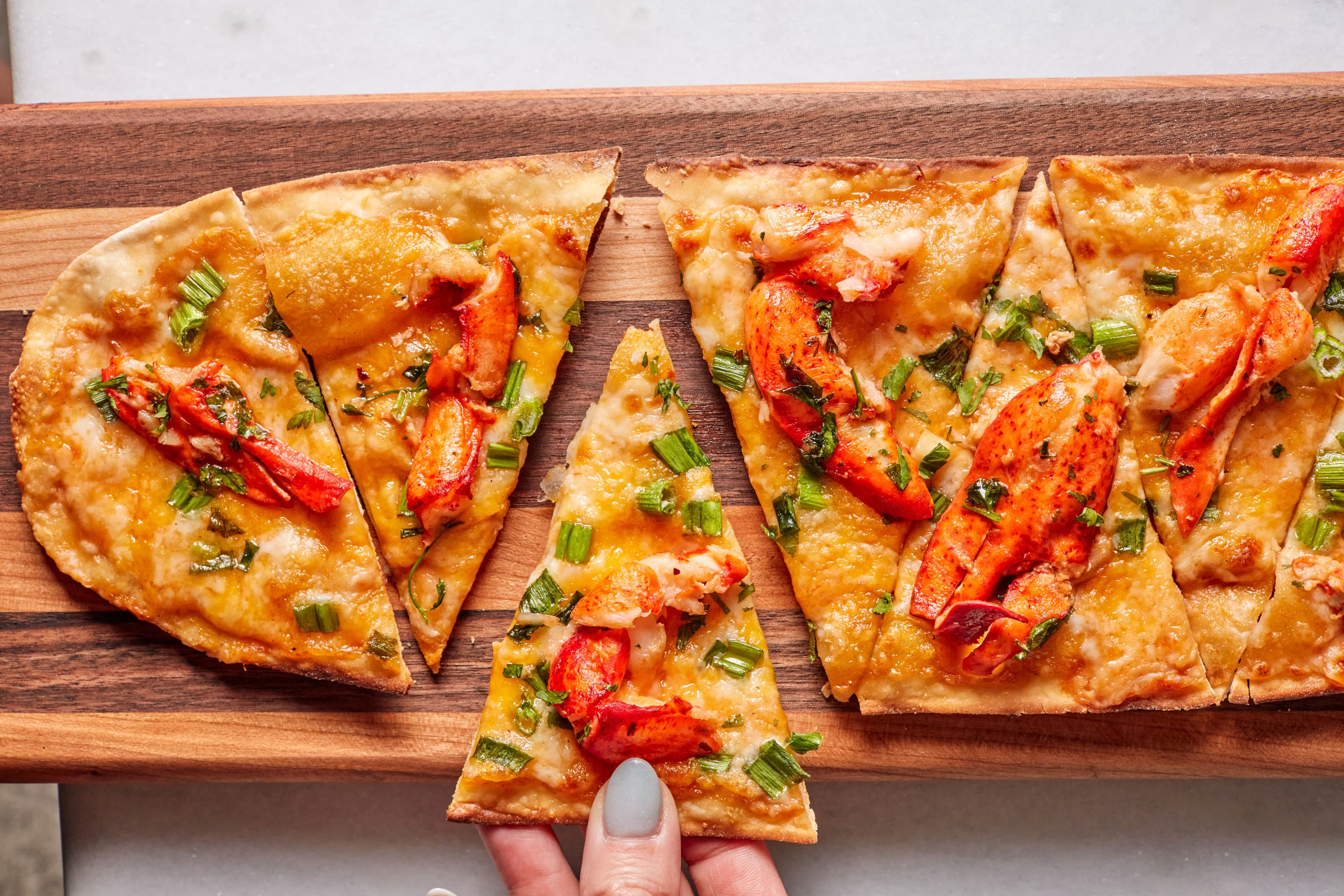 Lobster flatbread from Pinstripes on a wooden board, with a hand grabbing a slice.