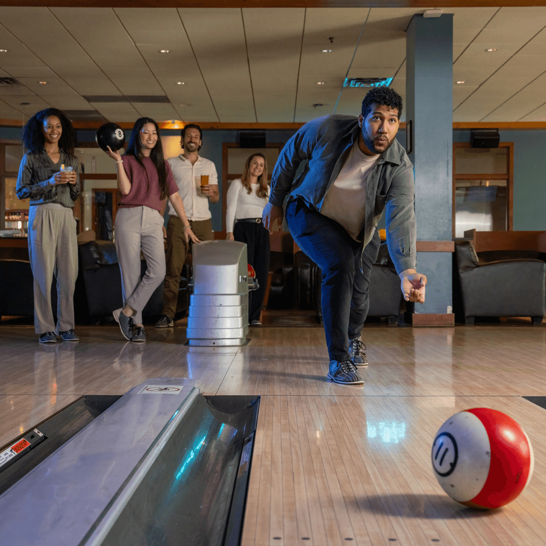 Man rolling a bowling ball down a lane while friends watch from behind.