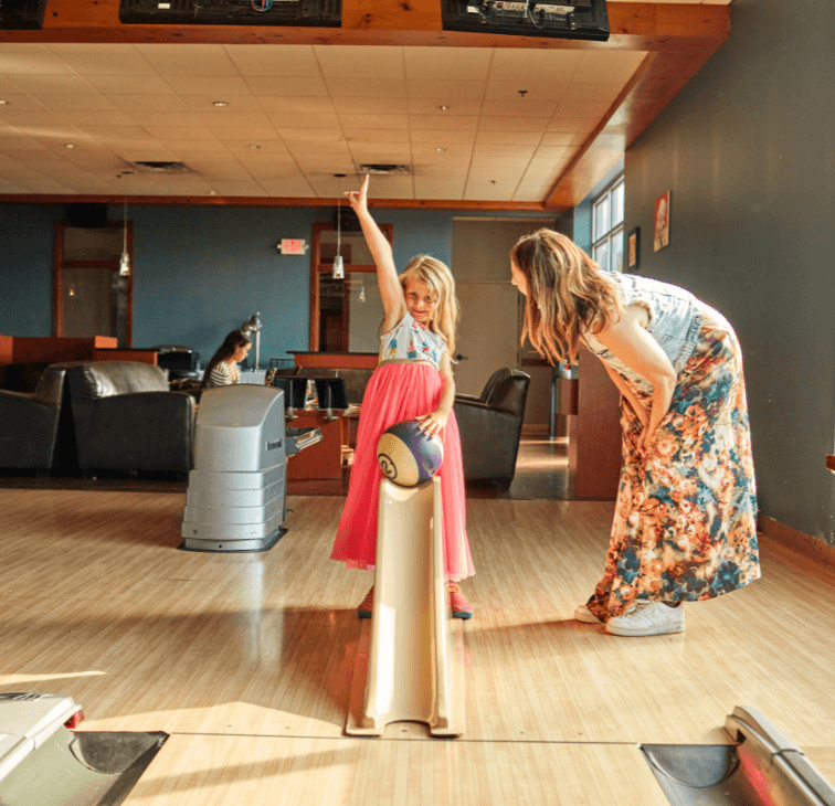 Young girl using a bowling ramp while her mother cheers on a Pinstripes lane