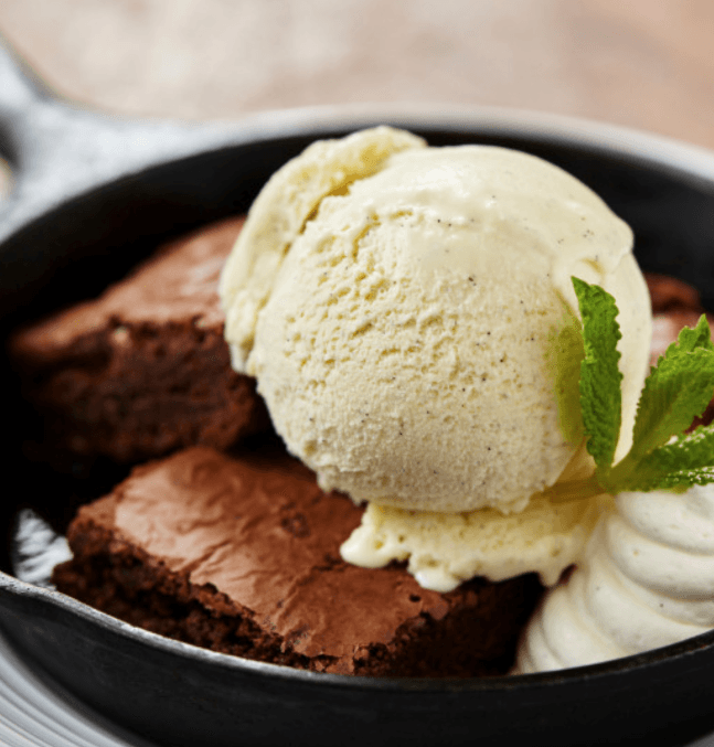 Warm brownie in a skillet topped with vanilla ice cream.